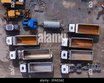 Luftaufnahme einer Asphaltfabrik mit verschiedenen BaulKW, Kipper und schweren Maschinen, die auf einem Schotterplatz in Danzig, Polen, geparkt sind. Stockfoto