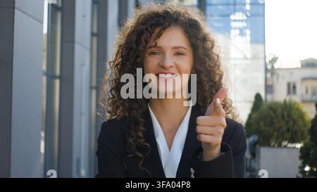 Porträt einer glücklichen, lächelnden, aufgeregten kaukasischen Geschäftsfrau, die eine Idee hat, aufgeregt aussieht, auf die Kamera zeigt und mit dem ‚Hey du‘-Gestus in der Stadt erscheint. Fröhlich Stockfoto