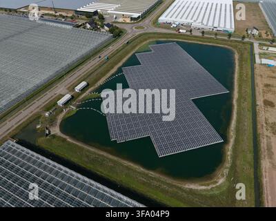 Luftbild einer großen schwimmenden Solarpanel-Anlage, die auf einem Teich installiert ist, umgeben von weitläufigen industriellen Gewächshäusern in den Niederlanden. Stockfoto