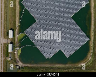 Luftaufnahme einer großen schwimmenden Solarfarm-Anlage, die auf einem ruhigen Teich installiert ist, mit Reihen von Photovoltaik-Panels, die Sonnenlicht reflektieren, umgeben von Grün Stockfoto