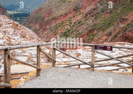 Blick auf die historischen Salzminen von Maras mit Verdampferteichen, die sich in den zerklüfteten Berghängen schmiegen, gesehen von hinter einem Holzzaun in Maras, Cusco, Peru Stockfoto