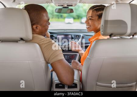 Schwarzes Paar sitzt auf den Vordersitzen eines Autos und lächelt sich gegenseitig an Stockfoto