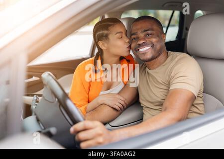 Liebendes junges afroamerikanisches Paar sitzt im Auto, Frau küsst die Wange des Mannes Stockfoto