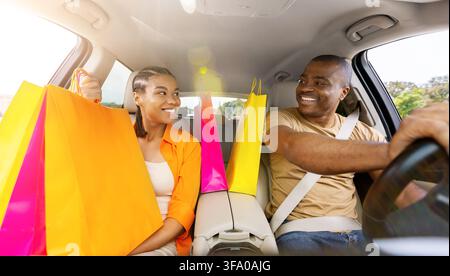 Fröhliches schwarzes Paar sitzt im Auto mit Einkaufstüten nach einem Einkaufstrip Stockfoto