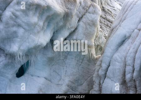 Gletschereisformationen mit texturierten Oberflächen, einer tiefblauen Eisgrotte, die sich öffnet, und zahlreichen tropfenden Eiszapfen, die eine gefrorene, abstrakte arktische Landschaft schaffen Stockfoto