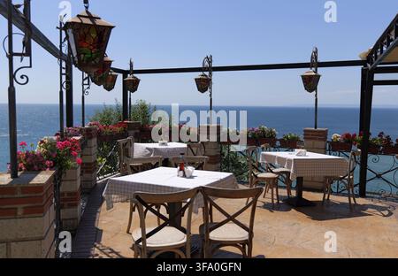 Leere Tische und Stühle auf einer Restaurantterrasse am Meer mit Blumenkästen und dekorativen Laternen unter einem klaren Himmel. Bulgarien, Kaliakra, 16. August 202 Stockfoto