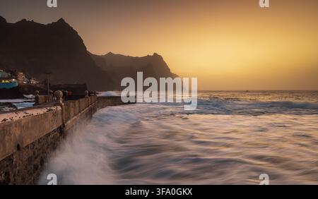 Blick auf die raue Küstenlinie von Santo Antao mit Wellen, die gegen die Steinmauer am Abend in Ponta do Sol, Ribeira Grande, Kap Verde schlagen Stockfoto