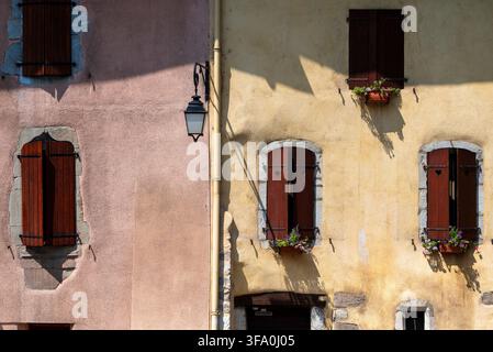 Bezaubernde rustikale pastellfarbene Fassaden mit braunen Holzfensterläden und Blumenkästen in einer französischen mittelalterlichen Stadt Stockfoto