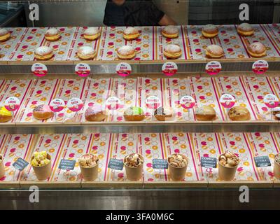 Vitrine gefüllt mit verschiedenen Gebäckstücken und Desserts. Jeder Artikel hat ein kleines Preisschild. Zu den Gebäckstücken gehören Donuts, Cupcakes und Eisbecher. Rückseite Stockfoto
