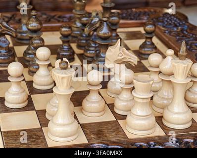 Schachset mit geschnitzten Holzfiguren auf kariertem Brett. Die Figuren umfassen König, Dame, Turm, Läufer, Springer und Bauer. Das Brett hat dunkle und helle Holzquadrate Stockfoto