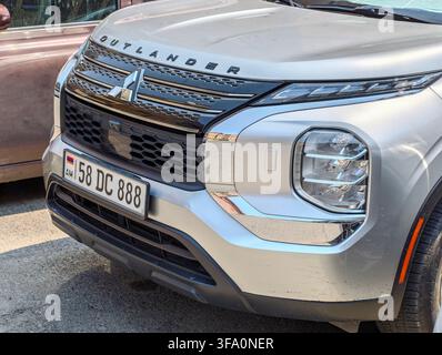 Vorderansicht eines silbernen SUVs mit sichtbarem Nummernschild. Das Fahrzeug hat moderne Scheinwerfer und einen Kühlergrill. In der Hintergrund sind ein Gehweg und ein Teil einer Wand sichtbar. Sonnenlicht Stockfoto