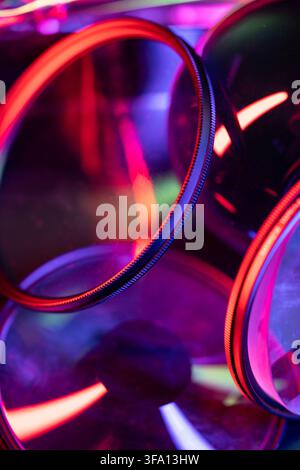 Nahaufnahme von überlappenden Kameralinsenfiltern mit lebhaften neonroten, violetten und blauen Reflexionen, die eine abstrakte futuristische Komposition für Photogra Stockfoto