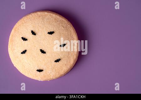 Hausgemachter Halloween-Keks, verziert mit schwarzen essbaren Fledermäusen auf einem lebendigen violetten Hintergrund. Minimalistische Top-Down-Komposition mit reichlich Kopierraum Stockfoto