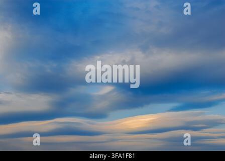 Panoramablick auf dramatische Linsenwolken, die glatte Wellenformen in einem lebendigen blauen Himmel mit einem sanften goldenen Sonnenuntergangsglanz bilden. Schöne natürliche Meteorolo Stockfoto