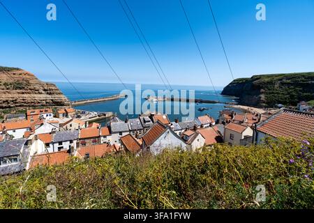 Hohe Aussicht über Staithes, North Yorkshire, mit den gedrängten Dächern und den gewundenen Straßen dieses historischen Fischerdorfs an einem hellen, sonnigen Tag Stockfoto