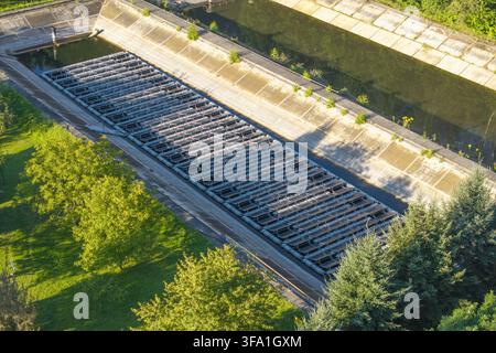 Luftaufnahme von schwimmenden Solarpanelen, die auf einem Wasserreservoir installiert sind, umgeben von grünen Bäumen und Betonwehern in Polen. Stockfoto