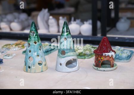 Handgefertigte glasierte Keramik-Christbaumkerzenhalter und Feenhaus, die auf einem Tisch in der Werkstatt stehen. Einzigartige handgefertigte Töpferdekorationen für Festtage Stockfoto