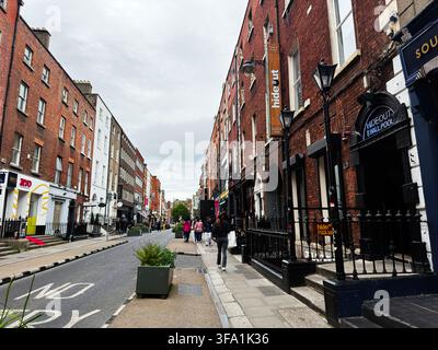Dublin, Irland - 22. Mai 2026: Urbane Straßenszene in Dublin mit Fußgängern, roten Backsteingebäuden, Geschäften und düsterem bedecktem Himmel. Stockfoto