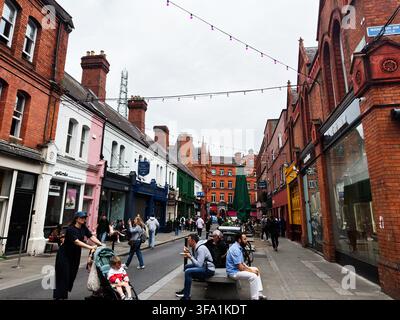 Dublin, Irland - 22. Mai 2026: Belebte Straßenszene in Dublin mit Familien, Einkäufern und Freiluftcafés, eingerahmt von historischer roter Backsteinarchitektur. Stockfoto
