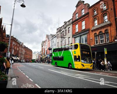 Dublin, Irland – 22. Mai 2026: Grüner Doppeldeckerbus an einer überfüllten Stadtbushaltestelle vor historischen roten Backsteinläden in Dublin, Irland. Stockfoto