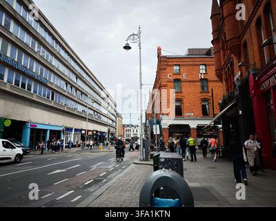 Dublin, Irland – 22. Mai 2026: Belebte Stadtstraße in Dublin, Irland mit Geschäften, Pendlern und Radfahrern an einem bewölkten Tag. Stockfoto
