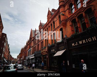 Dublin, Irland – 22. Mai 2026: Belebte Dubliner Straße mit roten Backstein-Viktorianischen Gebäuden, traditionellen Pub-Fassaden, Fußgängern und urbaner Atmosphäre. Stockfoto
