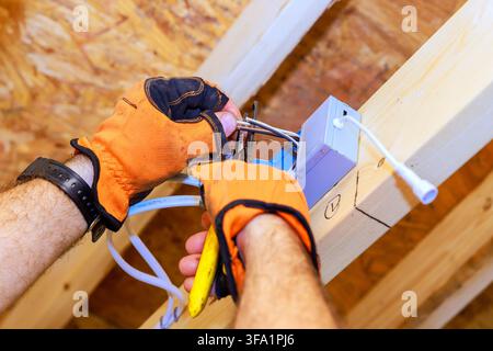 Der Bauunternehmer repariert elektrische Leitungen im Gebäude mit Werkzeugen, während er Handschuhe trägt und sorgfältig arbeitet. Stockfoto