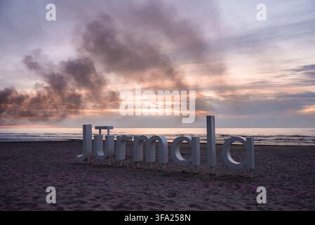 Großes Jurmala-Stadtzeichen steht bei Sonnenuntergang auf einem sandigen Strand in Lettland Stockfoto