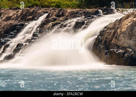 Ein konzentrierter Abschnitt des Tad Faek-Wasserfalls stürzt über dunkles, zerklüftetes Gestein in ein blaugrünes Becken. Stockfoto