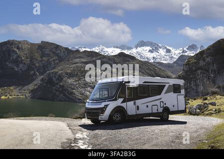 Blick auf die Seen von Covadonga mit einem modernen Wohnmobil, das auf einer Schotterstraße neben dem Wasser geparkt ist, mit schneebedeckten Bergen unter einem blauen Himmel in Astu Stockfoto