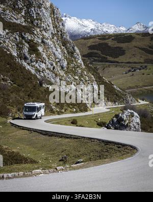 Blick auf ein Wohnmobil, das entlang einer kurvenreichen Bergstraße in der Nähe der Seen von Covadonga fährt, mit felsigen Klippen und schneebedeckten Gipfeln im Hintergrund in Ast Stockfoto