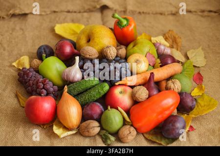 Eine reiche Herbsternte mit einer Auswahl an frischem Bio-Gemüse, rohen Früchten und Walnüssen, arrangiert auf einem rustikalen Sackleinen mit gefallenen Blättern Stockfoto