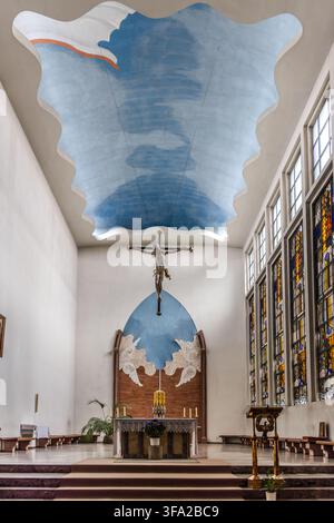 Der Chor der St.-Pius-Kirche in Köln-Zollstock. Das hängende Holzkreuz wurde vom Düsseldorfer Bildhauer Herbert Belau entworfen, einem Schüler von Ewald Mataré. Wilhelm Buschulte schuf ‚Das Tor zur Zukunft‘ an der Vorderwand des Chors. Köln, Nordrhein-Westfalen, Deutschland Stockfoto
