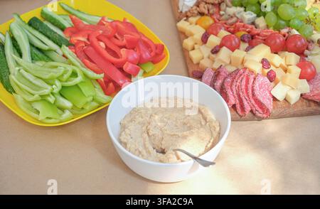 Kremiger Hummus serviert mit frischer Gurke, Paprika, Käse, Trauben und verschiedenen Vorspeisen auf einem Tisch. Buntes, mediterran inspiriertes Angebot für e Stockfoto