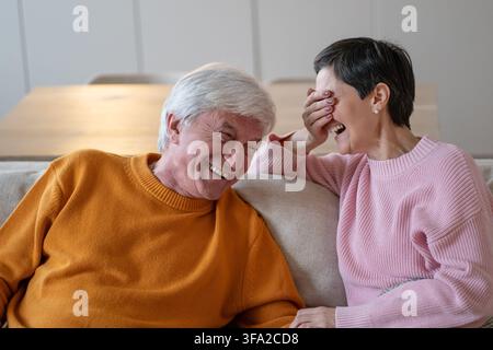 Positiver, unbeschwerter älterer Ehemann und Ehefrau, die zusammen zu Hause auf dem Sofa sitzen und lachen und scherzen Stockfoto