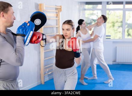 Frau, die Boxhandschuhe trägt, Übung und Schlag auf die Pads für das Boxen. Frau mit Trainer im Fitnessstudio Stockfoto