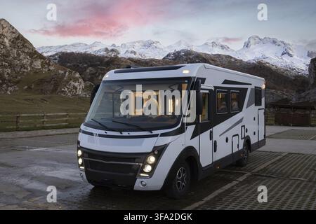 Blick auf ein modernes Wohnmobil, das in der Region der Seen von Covadonga geparkt ist, mit schneebedeckten Bergen und einem rosafarbenen Sonnenuntergangshimmel im Hintergrund in Asturien, Astur Stockfoto