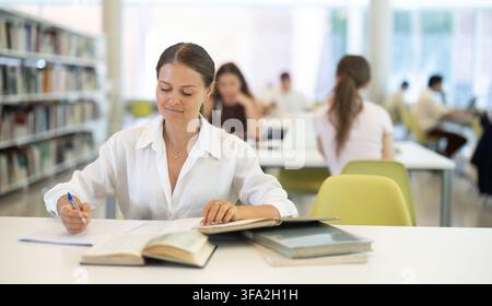 Studentinnen lesen Buch und machen Notizen in der Bibliothek Stockfoto