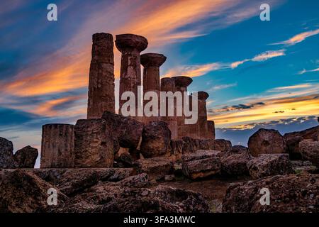 Ruinen des Herkulestempels bei Sonnenuntergang in Agrigento. Antike dorische Säulen und Steinruinen des Herkulestempels vor einem lebendigen Sonnenuntergangshimmel. Stockfoto