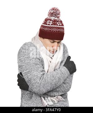 Eiskalter junger Mann mit Wintermütze und Schal, der sich zum Aufwärmen gegen einen weißen Hintergrund drückt Stockfoto