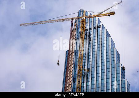 Gelbe Turmdrehkran neben moderner Glasfassade des im Bau befindlichen Wolkenkratzers 400 Lake Shore Drive unter bewölktem Himmel in Betrieb. Stockfoto