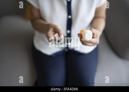 Reife asiatische Frau, die sorgfältig Medikamente hält, während sie die Anweisungen auf ihrem Handy liest Stockfoto
