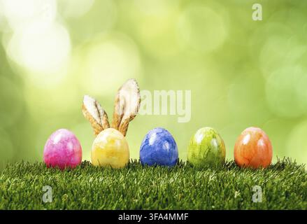 Eine Reihe von fünf bunten Ostereiern auf grünem Gras mit Hasenohren im Frühling Stockfoto