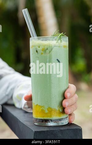 Hand, die einen gekühlten Matcha-Latte mit Mango und Rosmarin hält Stockfoto