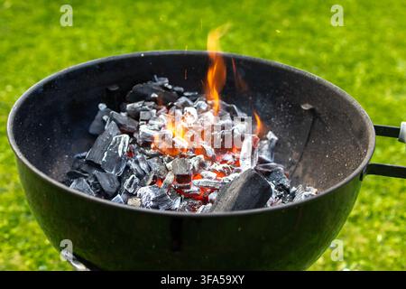 Heiß brennender Holzkohlegrill in einem Garten mit glühenden Kohlen und Flammen, vorbereitet für das Grillen im Freien, Sommergrillen, Picknick und Hinterhofversammlungen Stockfoto