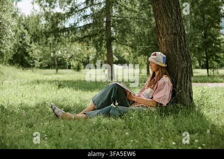 Frau sitzt unter einem Baum und skizziert während des Kunstunterrichts im Freien Stockfoto