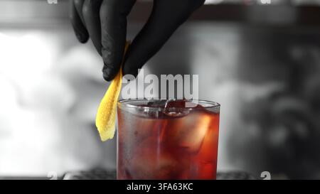 Barkeeper garniert Negroni-Cocktail mit Zitronenschale, bereitet alkoholischen Drink an der Bar für Kunden zu Stockfoto