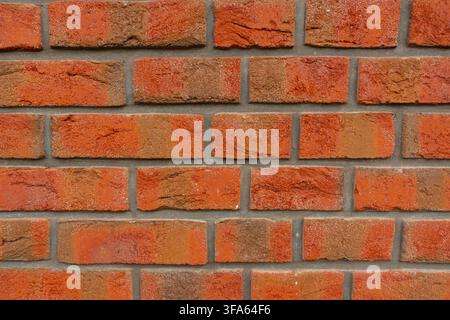Nahaufnahme einer verwitterten roten Ziegelwand mit verschiedenen orange-roten Tönen, rauer Mauertextur und grauen Mörtelnahtstellen Stockfoto
