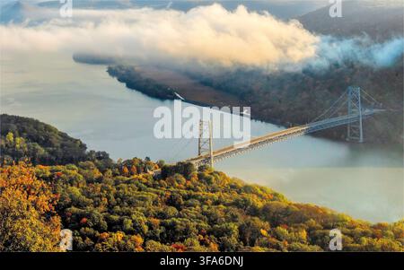 Luftaufnahme von Bear Mountain mit einer Brücke, die die Berge in New York State im Herbst mit bunten Bäumen und flauschigen Wolken überquert Stockfoto