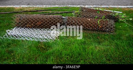 Mehrere Rollen Drahtzaun liegen auf dem Rasen, nachdem sie für die Installation eines neuen Zauns entfernt wurden. Stockfoto